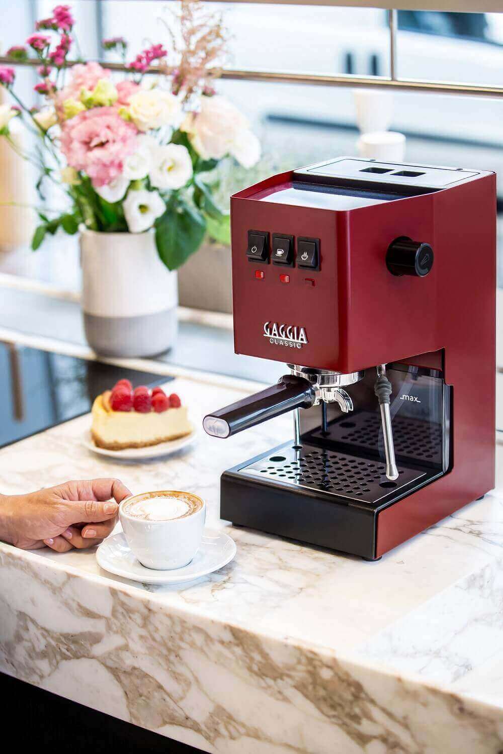 Gaggia New Classic in Sherry Red mit Blumen im Hintergrund Gaggia New Classic in Sherry Red mit Blumen im Hintergrund