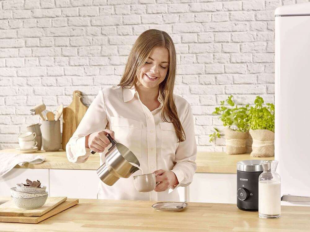 Frau, die Milchschaum in Cappuccino Tasse einschenkt mit Severin Milchaufschäumer Spuma Frau, die Milchschaum in Cappuccino Tasse einschenkt mit Severin Milchaufschäumer Spuma