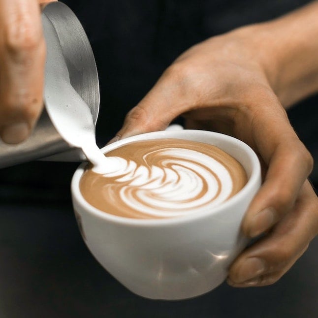 Barista schenkt Milchschaum mit Milchkännchen in Tasse Barista schenkt Milchschaum mit Milchkännchen in Tasse